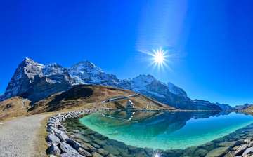 Lake Fallboden near Kleine Scheidegg is bathed in bright sunshine. In the background, the Eiger, Mönch, and Jungfrau rise up.