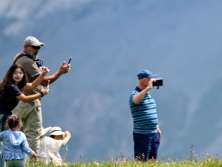 Plusieurs personnes se tiennent dans un alpage verdoyant et prennent en photo une vache solitaire. Cette scène illustre la découverte par les visiteurs de l'économie alpestre traditionnelle.