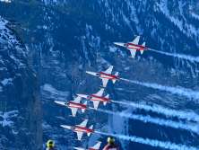 Jets der Patrouille Suisse fliegen in enger Formation über das Lauberhornrennen. Im Vordergrund stehen Zuschauer auf einem verschneiten Hang und verfolgen die Flugshow, während die Flugzeuge ihre Rauchspuren vor der steilen, schneebedeckten Bergflanke ziehen.