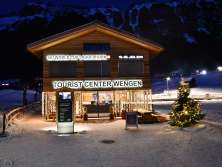 Le centre d'information touristique est brillamment éclairé en cette soirée d'hiver à Wengen. Un sapin de Noël illuminé trône devant le bâtiment.