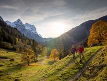 Two hikers are out and about in the Rosenlauital valley. There is an autumnal atmosphere, and the sky is covered with light, hazy clouds. The mountain panorama is cloaked in snow.