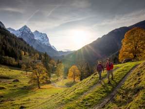 Zwei Wanderer unterwegs in der Landschaft vom Rosenlauital. Es herrscht eine herbstliche Stimmung und der Himmel ist mit leichten Dunstwolken bedeckt. Das Bergpanorama hat einen verschneiten Umhang.