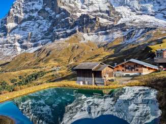 The Kleine Scheidegg mountain restaurant is located above a small mountain lake. In the background rise the Eiger and the Mönch, whose striking rocky and snow-covered slopes are reflected in the calm water.