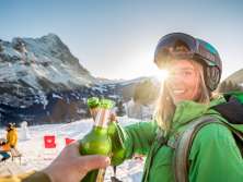 Die Wintersportlerin geniesst nach einem schönen Tag im Schnee ein verdientes Bier im Sonnenuntergang. Die Sonne beleuchtet mit ihren letzten Strahlen den Eiger.