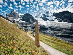 An early summer view of the Kleine Scheidegg station, with a view of the Jungfrau. The mountains are covered in glaciers. The Jungfrau Eiger Walk hiking trail can be seen in the foreground.